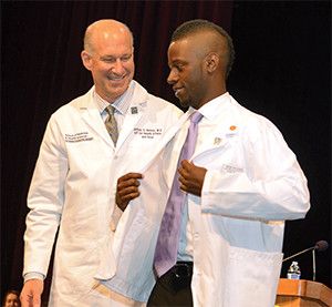 Dean Jeffrey Akman presenting student with white coat