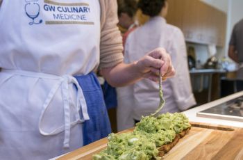 A woman with an apron that reads "GW Culinary Medicine" prepares food
